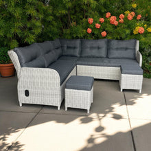 Outdoor patio sectional with gray cushions and ottoman on a patio with plants and flowers in the background.
