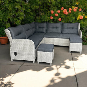 Outdoor patio sectional with gray cushions and ottoman on a patio with plants and flowers in the background.