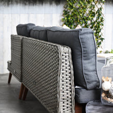 Gray cushioned outdoor sofa with wicker backrest in a garden setting