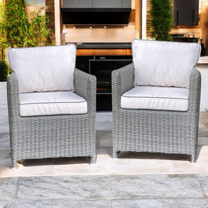 Two gray wicker armchairs with beige cushions on a patio.