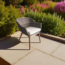 Wicker chair with a cream cushion on a stone patio - DECOR STAR